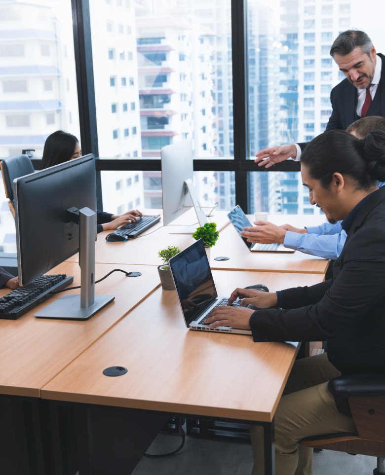 Group of diversity business people working with desktop computer and laptop after meeting finished but their manager standing still advise to some colleagues at the office